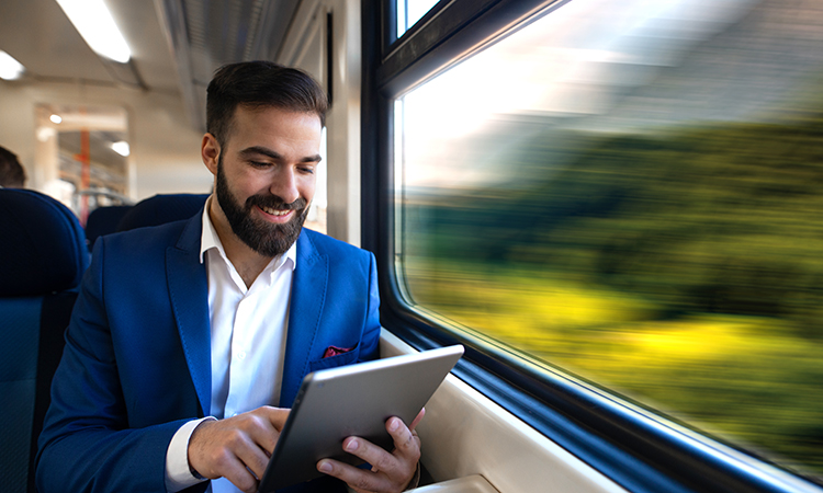 商人坐在窗边看新闻，在他的平板电脑上上网，而在舒适的高铁旅行。