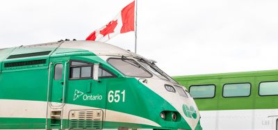 开往多伦多的Metrolinx GO运输公司动力工业公司651号火车头拉着一列通勤列车通过一个车站，经过一面加拿大国旗。