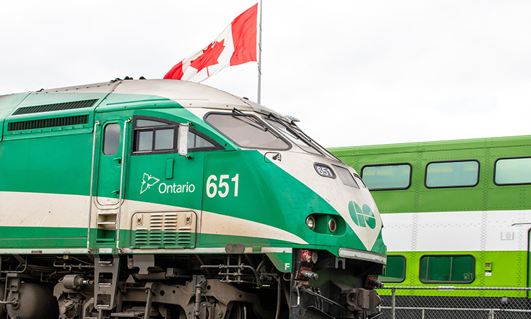前往多伦多的Metrolinx GO交通动力动力工业公司的651号机车牵引着一列通勤列车穿过一个车站，经过一面加拿大国旗。